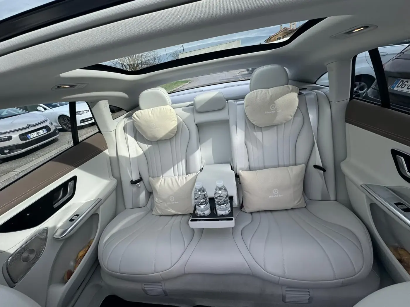Places arrière de la Mercedes EQE de Toulouse VTC Pro — banquette cuir clair, coussins Mercedes-Benz, toit panoramique et bouteilles d’eau offertes